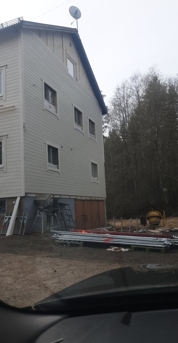 Hus under renovering med byggmaterial och stegar utanför.