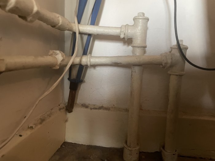 Värmeelement med synliga rörledningar och tecken på vattenläckage vid fogar mot en vägg.