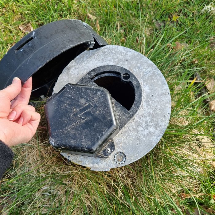 Sprucket lock på en brunn med en hand som håller i en del av det brutna locket, gräs i bakgrunden.