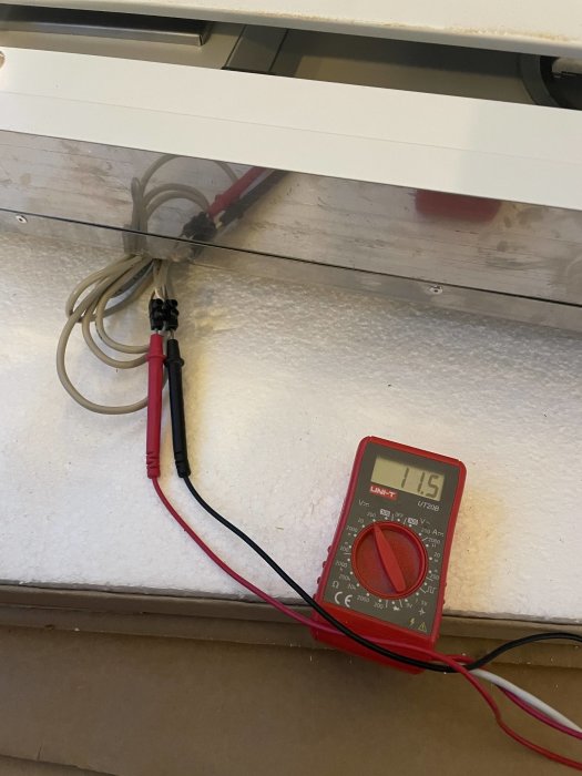 Digital multimeter visar 11.5V kopplat till kablar vid en enhets styrpanel under installation.
