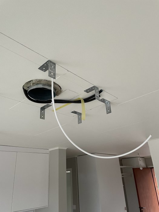 Installation av baldakin för köksfläkt med synligt ventilationsrör och fästelement i taket.