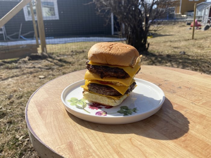 Dubbel cheeseburgare på en tallrik utomhus med en bakgård i bakgrunden.