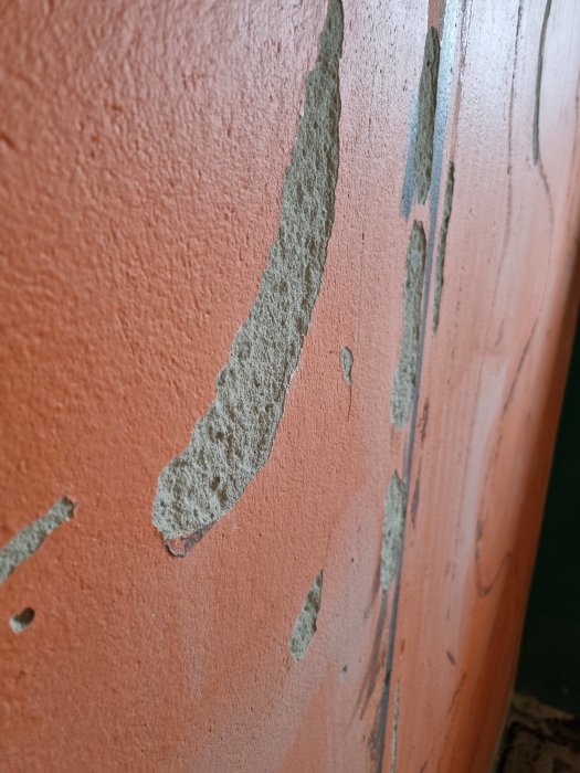 Orange innervägg med skador och bortfall av puts efter väggskivor, överflata synlig.