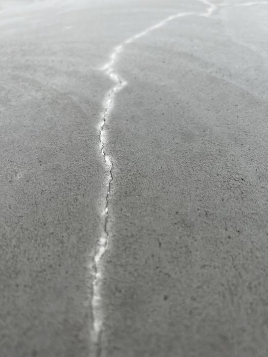 Spricka i en nyligen gjuten betongplatta, med fokus på en längsgående ytspricka.