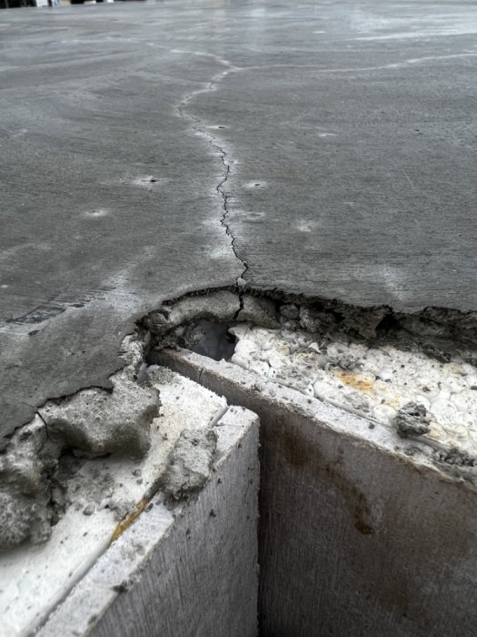 Nyggjuten betongplatta med sprickbildning och avskalning vid kanten, indikerar potentiell skada.
