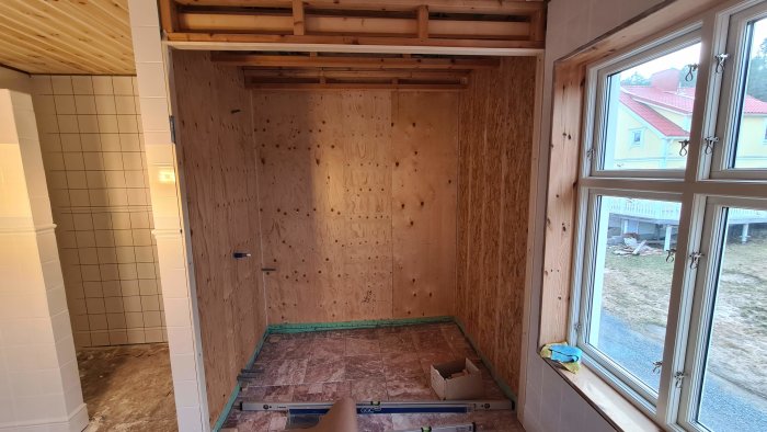 Underkonstruktion av bastu med isolering, träpaneltak och plywoodväggar, nära fönster och kaklat badrum.