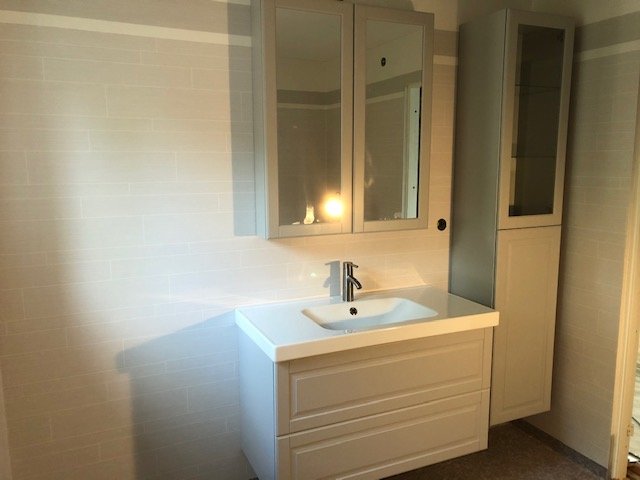 Renoverat badrum med vita kakelväggar och handfat med underskåp samt spegelskåp ovan.