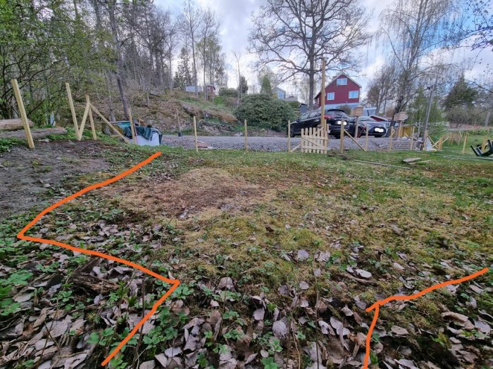 Trädgårdsmark med föreslagen körväg markerad med orange pil, platt mark och en låg mur i ett bostadsområde.