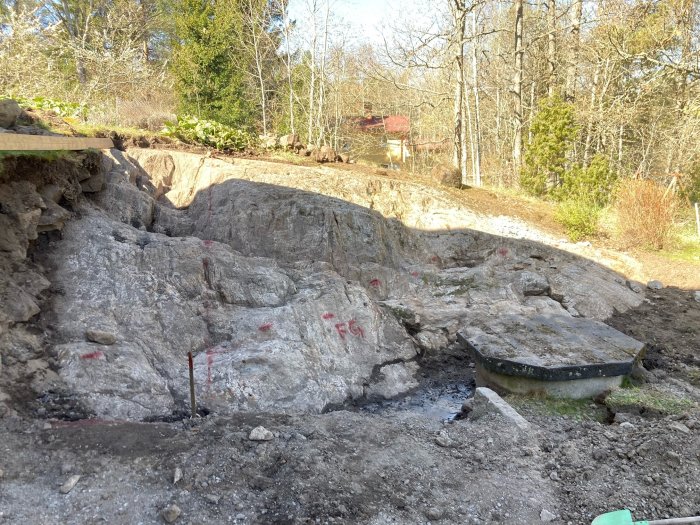 Bild på ett stort tvättat bergsutsprång markerat med röda streck, förberett för grävarbete inför en tillbyggnad.