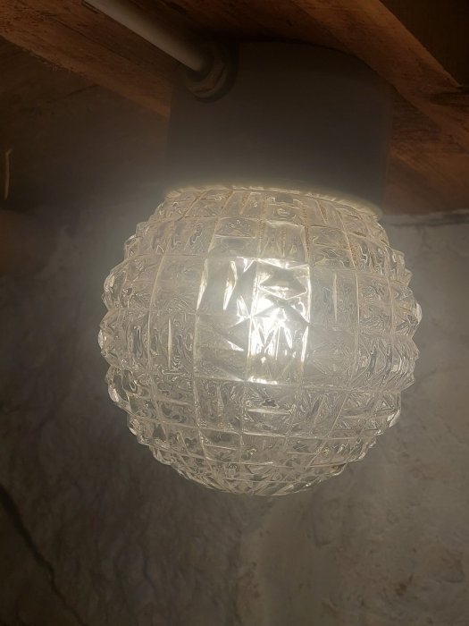Klar mönstrad lampglob hängande under ett träbjälke.