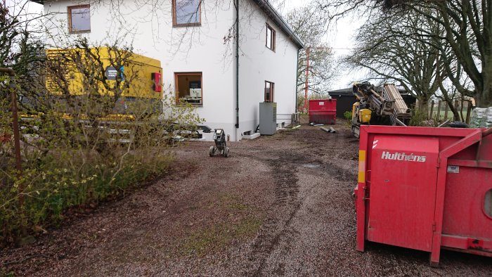 Gräsmatta med spår av kalkhaltigt vatten och högt gräs, byggutrustning och en container i bakgrunden.