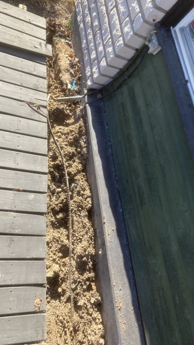 Gammal kabel dragen längs en husvägg och ovan jord nära en grusad gångväg.