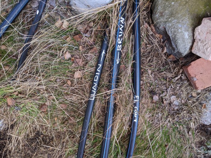 Kabelrör märkta med hemmagjorda etiketter från kakburkar och buntband på gräsmark.