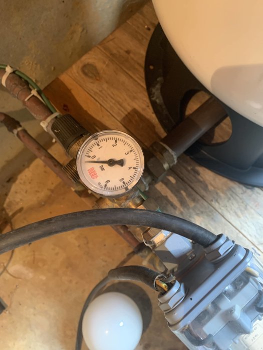 Manometer visar tryck vid VVS-installation nära en vit behållare och rörledningar.