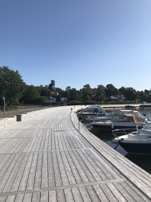 Träbrygga behandlad med Organowood i Djursholm, med båtar förtöjda vid sidan och grönska i bakgrunden.