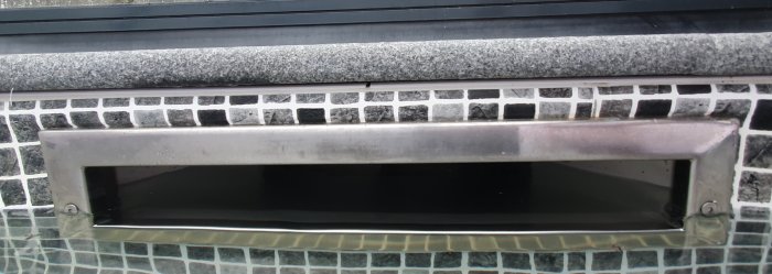 Bräddavlopp på en pool med en stensarg och mosaikplattor synlig strax ovanför vattenytan.