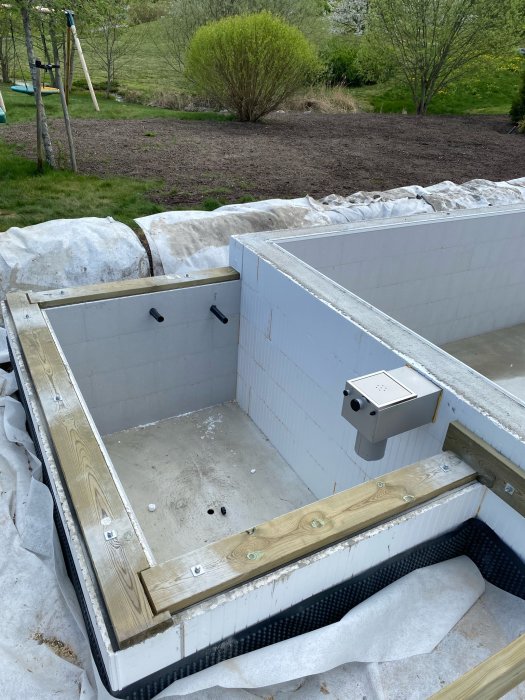 Pågående poolbygge med grå kantsten och vita kakelväggar, omgivet av en trädgård i Sigtuna.