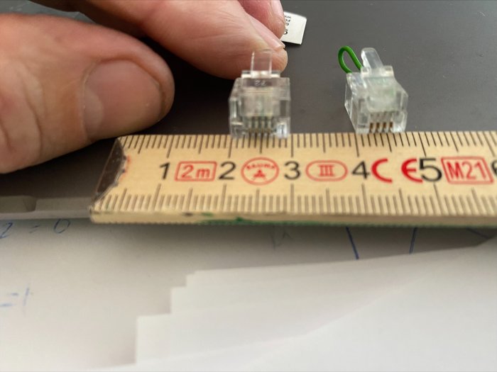 Två telefonkontakter bredvid varandra ovanpå en linjal som visar deras storlek, RJ-9 bredvid en trolig RJ-11.