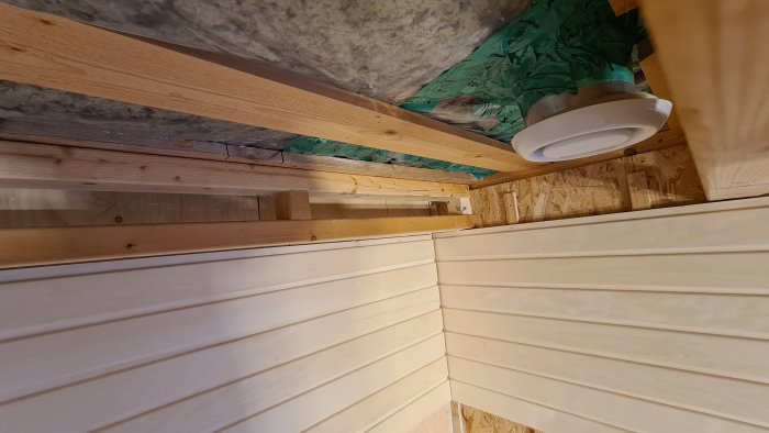 Ventilationssystem ovanför bastu med synlig frånluftsventil, isolering och träpanel.