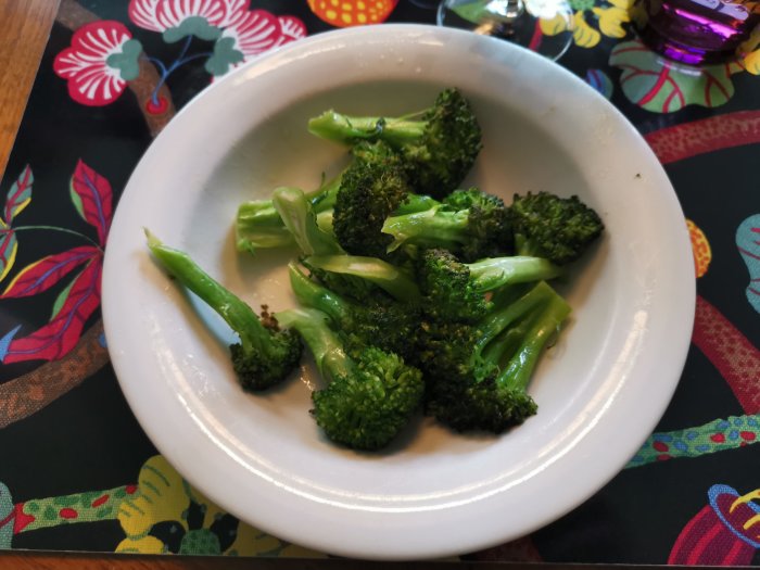 Smörstekt broccoli al dente på en vit tallrik med färgglad duk i bakgrunden.