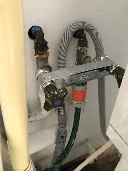 Hemmabyggd kranfastsättning med flexibla slangar och kopplingar mot vägg.