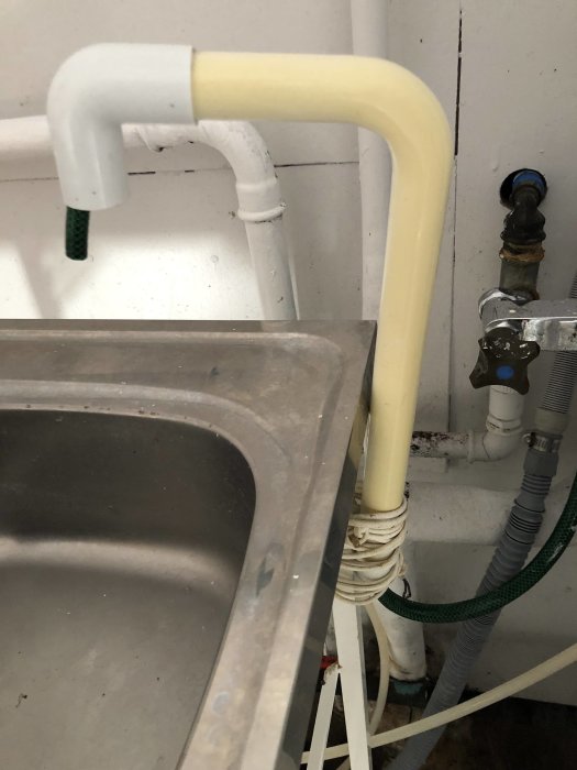 Hemmabyggd kran av PVC-rör ovanpå vask mot vit vägg och ansluten till befintlig vatteninstallation.