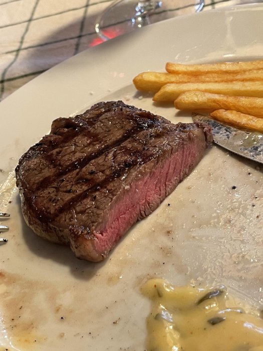 Mediumstekt spansk entrecôte på tallrik med friterade pommes och bearnaisesås, bord i bakgrunden.