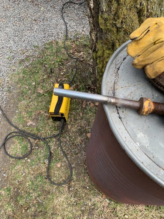 Gängad stång anpassas med fil och mutterdragare vid improviserad arbetsstation utomhus.