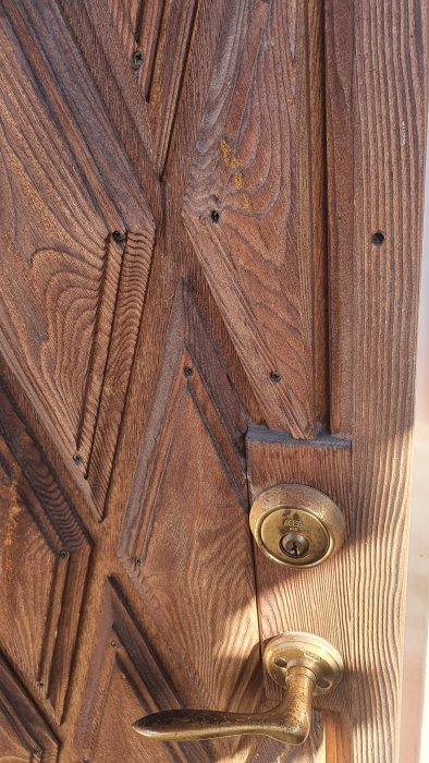 Gamla träytterdörr detalj med handtag och lås, behov av målning eller oljebehandling.