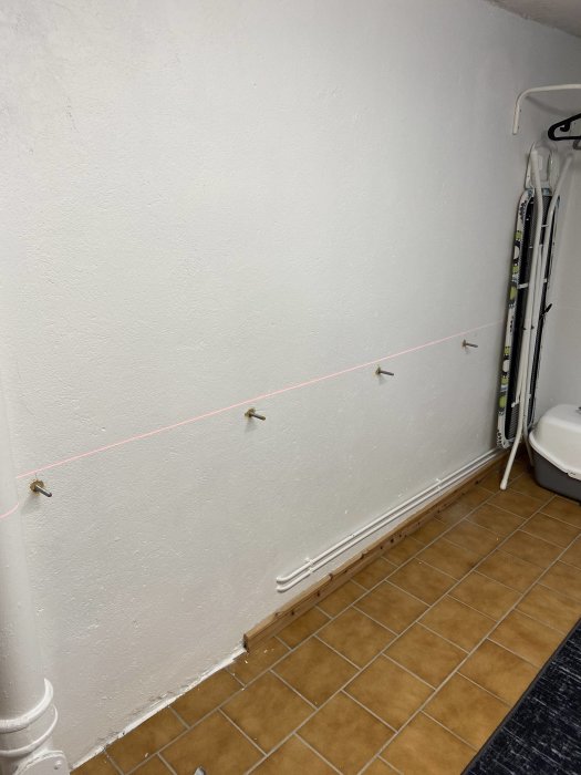 Vägg med kemankare och laserlinje som visar var konsoler ska skruvas upp, ojämnt golv syns.
