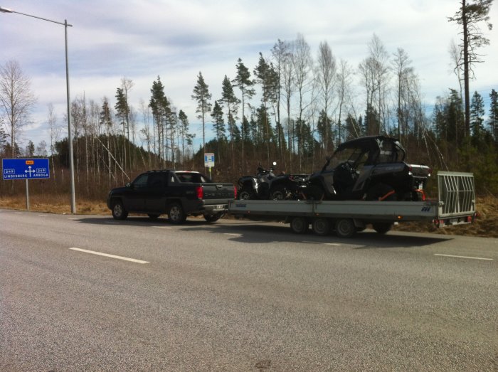 Chevrolet Avalanche 2002 drar en släpvagn med snöskoter och motorcyklar på en väg.