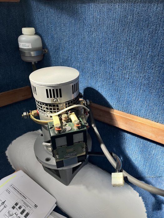 Marinelektrisk motor monterad på båtens blåa sidopanel, instruktionsbok på grått underlag.