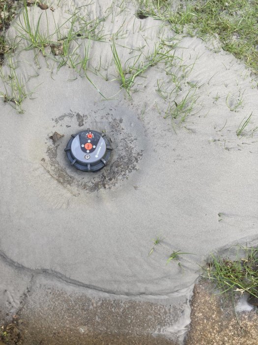 Sprinklerhuvud omgivet av sand och vatten med gräs runt kanterna efter att systemet tömts.