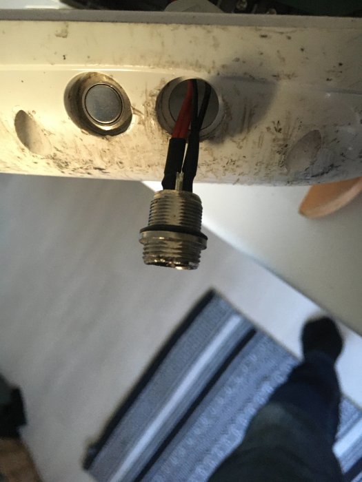Trekontakts laddaruttag på en hoverboard med en röd och svart kabel ansluten, på smutsig yta.