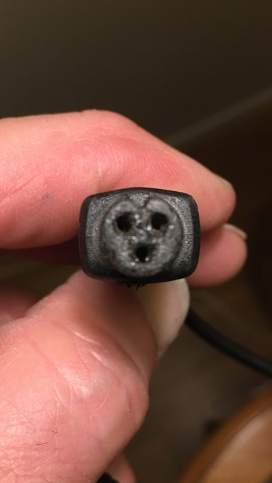 Närbild på hand som håller en kontakt med två hål och en pin, möjligtvis pluspolen markerad överst till vänster.