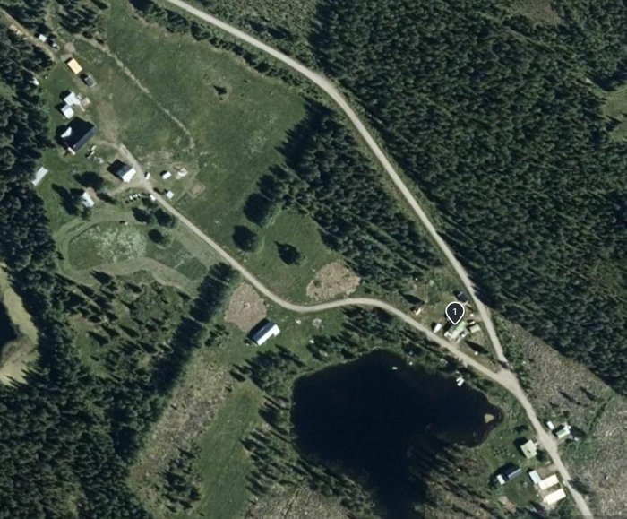 Flygbild av landskap med befintlig grusväg bland bebyggelse och skog, planerad vägomläggning indikeras ej i bilden.