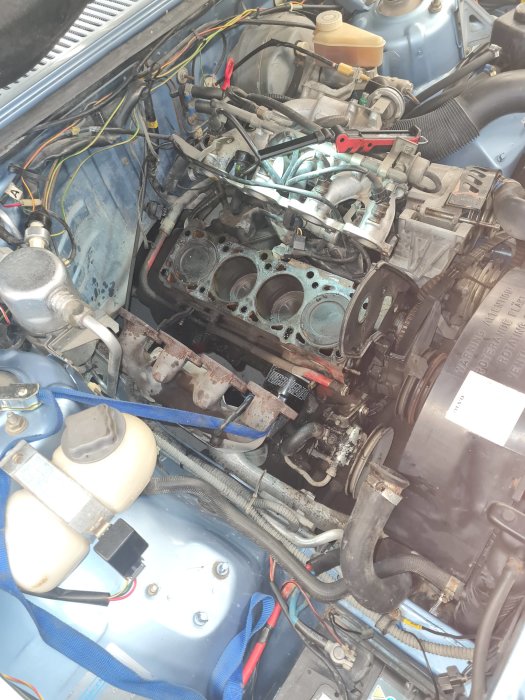 Motor i bil med avlägsnat topplock och exponerade motorblocket, diverse verktyg och motorrekvisita synliga.