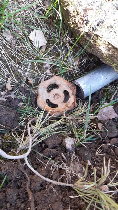 Gammal rostig kran med rundat rött vred och 25 mm slang, ligger på jordig mark med gräs.