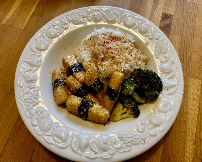 Tallrik med friterad tofu inlindad i nori, ris och broccoli, toppad med sesam och chilisås.