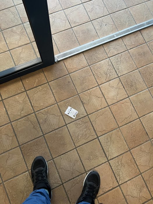 Person står framför en öppen dörr med en lapp på ett kaklat golv.