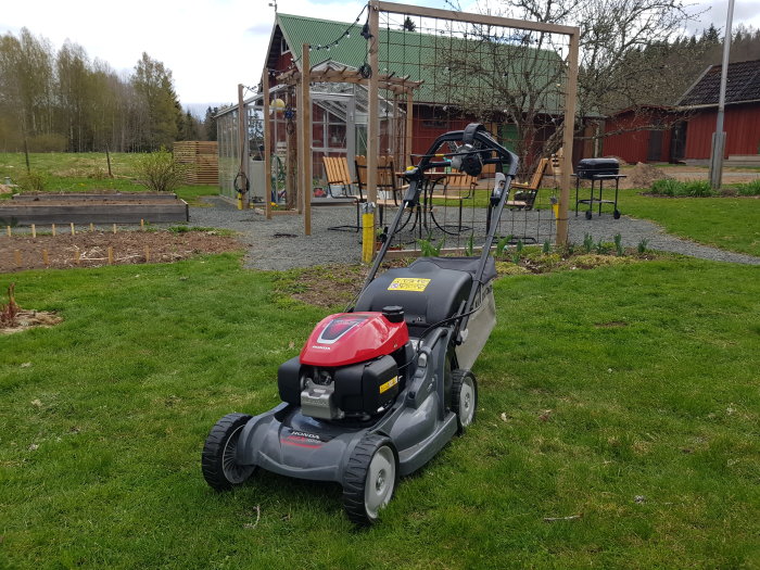 Honda gräsklippare i en trädgård med trädgårdsland och lekställning i bakgrunden.