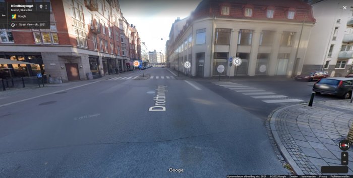 Stadsgata med flera oskyltade korsningar och vägmarkeringar, stoppskylt syns på en korsande gata.