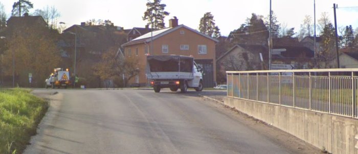 Gata utan skyltar med ett lastfordon och en sopbil, samt räcke på höger sida.