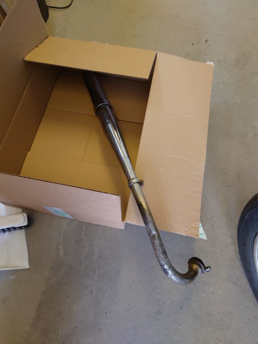 En bågformad metallstång som sticker ut ur en brun kartong på ett betonggolv.