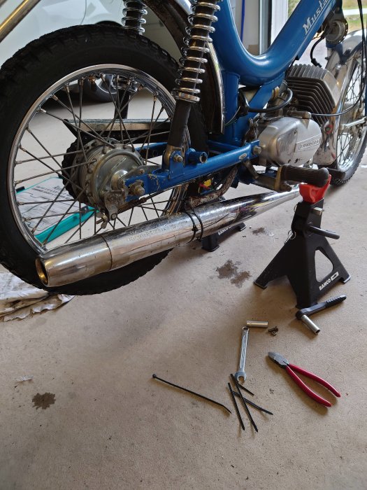 Motorcykel på stöd med verktyg och oljefläck på betonggolv.