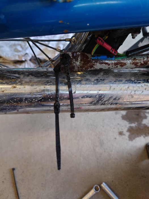 En svetsad stötdämparfäste på en motorcykel med synliga svetsskarvar och kablar.