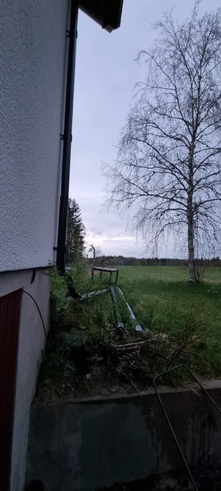 Husets hörn med stuprör och kabel vid marken som kan användas för att leda bort backspolningsvatten.