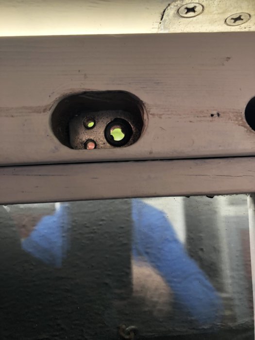 Närbild av dörrens låskista med urtag för låscylinder och handtag, reflektion av en person syns.