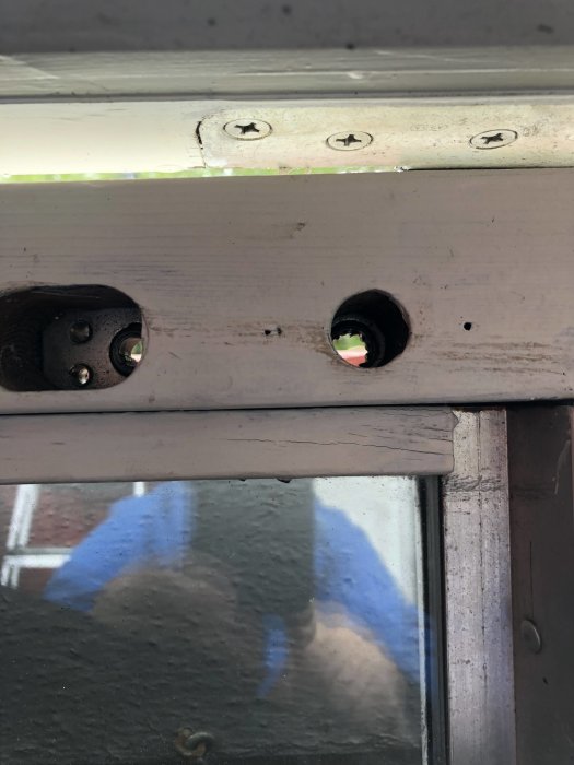 Detalj av fönsterkarm med borrhål och fästelement, reflekterande glas synligt.