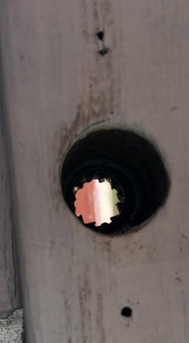 Låsbar spanjolett med udda formad tryckesroddare synlig i dörrens fyrkantshål.